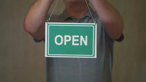 A man hangs an open sign on the front door Stock Footage 246795401