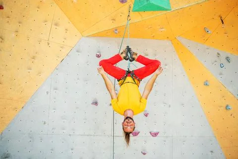 A man hangs upside down in a lotus position on a climbing wall Stock Photos