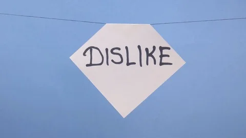 A man hangs a white sheet of paper with a black inscription dislike on a blue Stock Footage 123785602