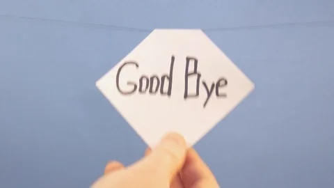 A man hangs a white sheet of paper with a black inscription good bye on a blue Stock Footage 123785849