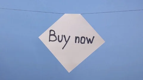 A man hangs a white sheet of paper with a black inscription "buy now" on a blue Stock Footage 123859019