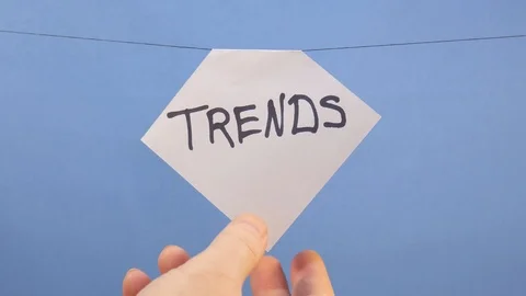A man hangs a white sheet of paper with a black inscription "trends" on a blue Stock Footage 124173285