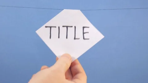 A man hangs a white sheet of paper with a black inscription "title" on a blue Video stock 124174103