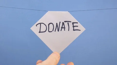 A man hangs a white sheet of paper with a black inscription "donate" on a blue Stock Footage 124203256