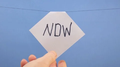 A man hangs a white sheet of paper with a black inscription "now" on a blue Stock-Footage 124203451