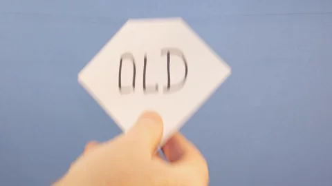 A man hangs a white sheet of paper with a black inscription "old" on a blue Stock Footage 124203503