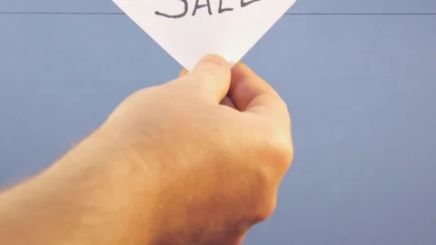 A man hangs a white sheet of paper with a black inscription "sale" on a blue Stock Footage 124203624
