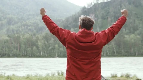 A man happily raises his hands up at the end of a difficult hiking route. Stock Footage 112004588