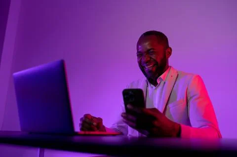 The man is happy at the computer. a dark-skinned man works in the evening off Stock Photos