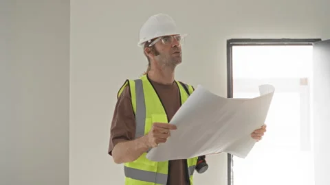 Man in hard hat and reflective vest holding blueprints and looking up insid.. Stock Footage 337375950