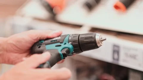 Man in a hardware store chooses a new screwdriver or drill next to a showcase of Video stock 279550638