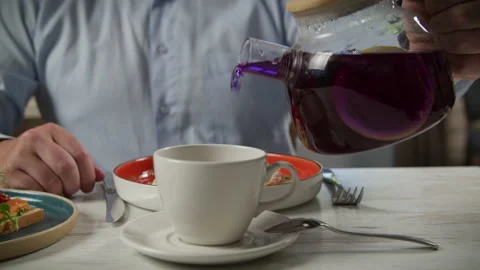 A man has breakfast in a cafe, pours tea from a teapot into a cup Stock Footage 204018282