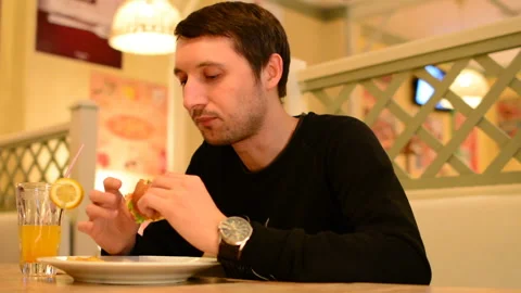 A man has a Burger in a restaurant and drinks lemonade Stock Footage 89130242