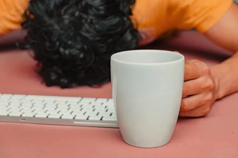 Man has burn out at work. Head, keyboard, smart phone and coffee on pink tabl Stock Photos