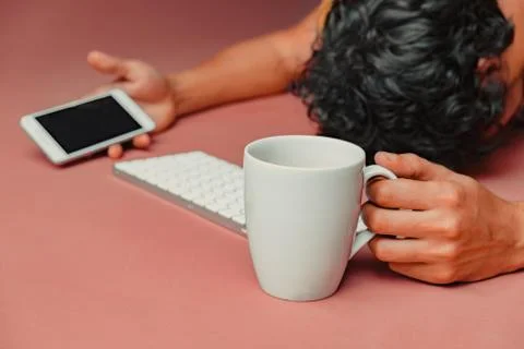 Man has burn out at work. Head, keyboard, smart phone and coffee on pink tabl Stock Photos