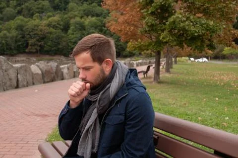 Man has cold or flu.  Man has catch cold is sitting on bench in the park Stock-Fotos