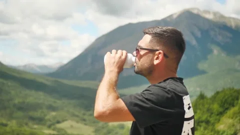 A man has reached the top of a mountain and is drinking from a plastic bottle Stock Footage 207050936