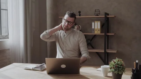 A man has a sore neck after hard work at a table with a laptop. pain in the neck Video stock 133339663