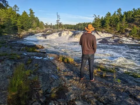 A man in hat admiring the view of a waterfall during sunset in the wilderness Foto stock