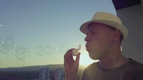 Man in a hat, against the background of the sunset blowing soap bubbles Stock Footage 303816902
