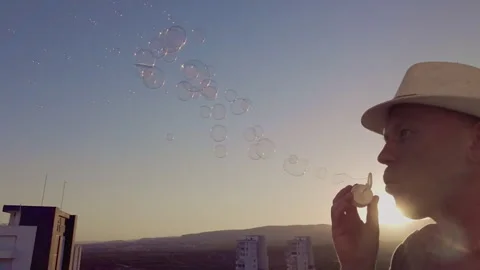 Man in a hat, against the sky at sunset blowing soap bubbles, side view Stock Footage 276277647