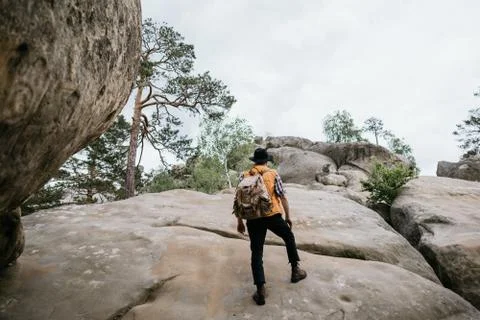 A man in a hat and a backpack climbs a rock. Extreme tourism Stock Photos