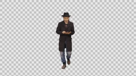 A man in a hat and coat walks &amp; using smartphone, 4k shot with alpha channel Video stock 68158901