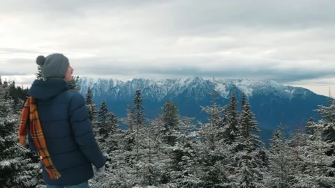 Man in hat and down jacket with scarf walks through forest in mountains, winter Stock Footage 234860519
