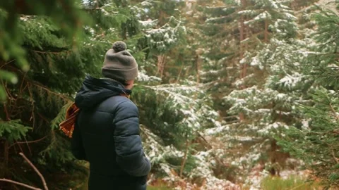 Man in hat and down jacket with scarf walks through forest in mountains, winter Stock Footage 234860697