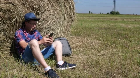 A man in a hat and glasses sits next to a table and looks at a smartphone. Stock Footage 135458236