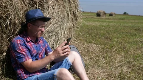 A man in a hat and glasses sits next to a table and looks at a smartphone. Stock Footage 135458255