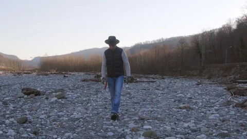A man in a hat and gloves with an axe is walking along the Bank of a mountain Video stock 123210598