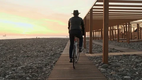 A man in a hat and a leather jacket rides a Bicycle along the embankment near a Stockbeeldmateriaal 121888095