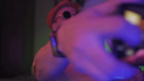 Man in hat ands sunglasses in the dark semi lit neon light room smoking hookah Stock Footage 130064235