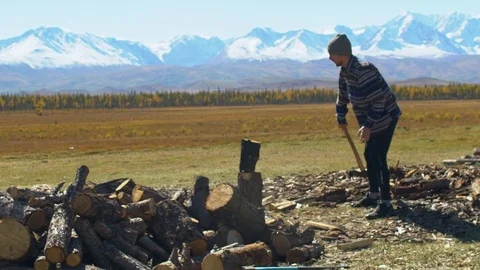 Man in hat with axe chopping firewoods in mountains. Guy with axe Stock Footage 101275822