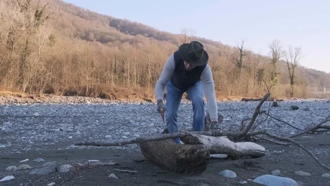A man in a hat with an axe cuts a dry branch for a fire. A man is a woodcutter Stock Footage 123300551