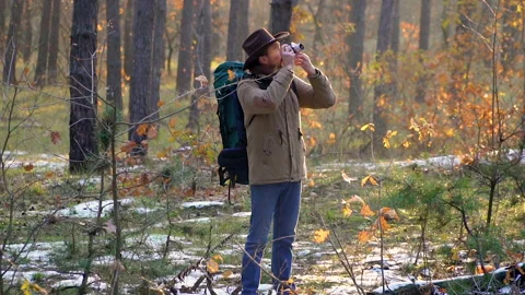 A man in a hat with a backpack takes pictures in the forest Stock Footage 143894496