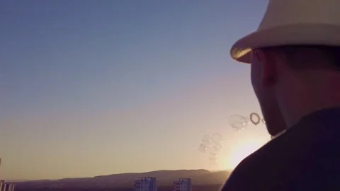 Man in a hat blowing soap bubbles, against the background of the sunset Stock Footage 263935564