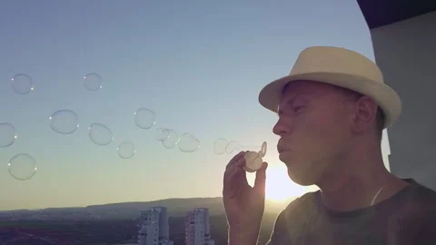 Man in hat, blowing soap bubbles against sunset, side view, copy space Stock Footage 280140580