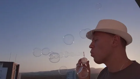 A man in a hat blowing soap bubbles, on the background of the sky at sunset Stock Footage 305229322