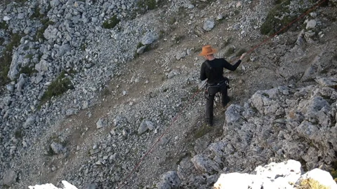 A man in a hat down the mountain on a rope. Stock Footage 97706042