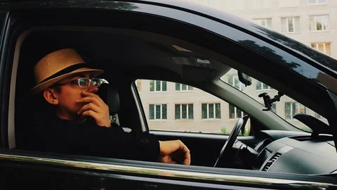 Man in hat, glasses sitting in car and touching mustache. Summer day. Parody Video stock 75313996