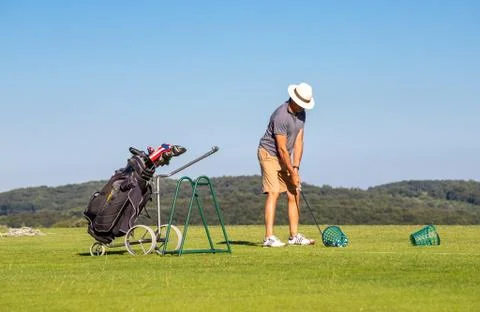 A man in a hat on a golf course preparing to hit the ball standing in front o Stock Photos