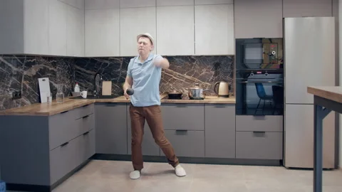 Man in a hat having fun in the kitchen while cooking, dancing and singing with a Stock Footage 167441170