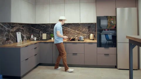 Man in a hat having fun in the kitchen while cooking, dancing and singing with a Stock Footage 167980159