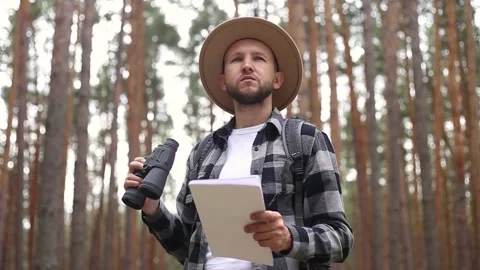 Man in a hat holds a map in and looks through binoculars while hiking Video stock 149946618