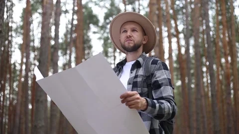 Man in a hat holds a map while hiking in the forest. Orientation concept, Stock Footage 149946607