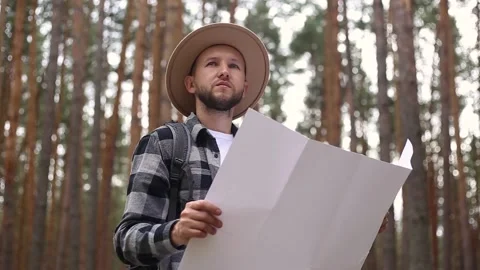 Man in a hat holds a map while hiking in the forest. Orientation concept, Stock Footage 149946608