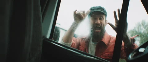 Man with hat knocks on car window waving and laughing Stock Footage 203584969