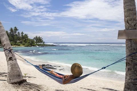 Man with hat, laying on blue hammock under palm trees at the beach Stock Photos